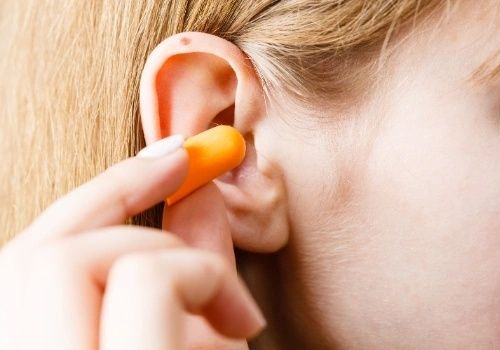 Lähikuva oranssin korvatulpan asettamisesta korvaan