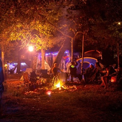 Festivaalileiriläisiä istumassa nuotion ympärillä telttojen keskellä yöllä